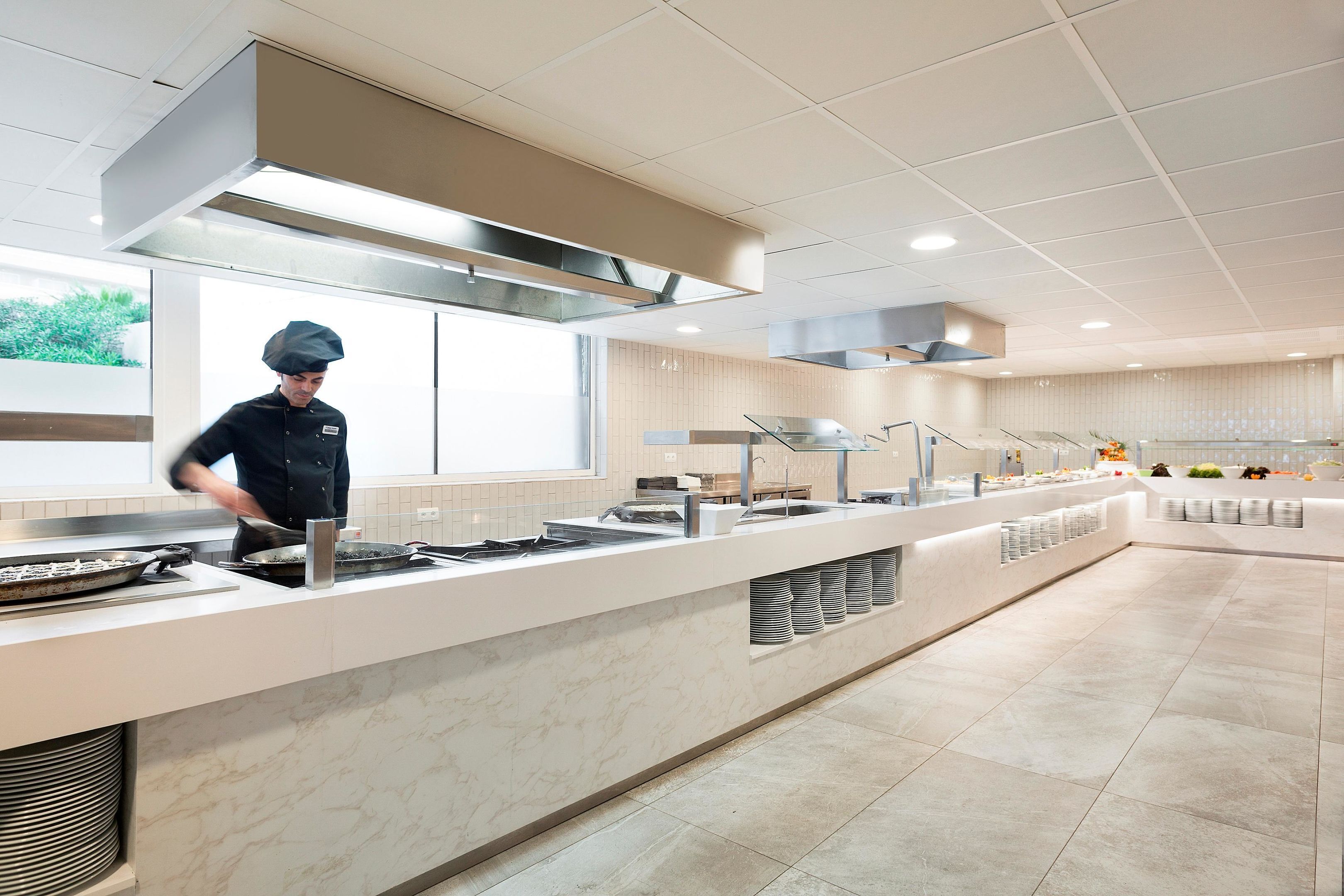 Una cocina moderna con un chef preparando comida, una barra larga con dispensadores de alimentos y un piso limpio con azulejos.
