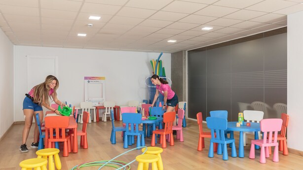 Una habitación con suelo de madera, varias mesas y sillas de colores.