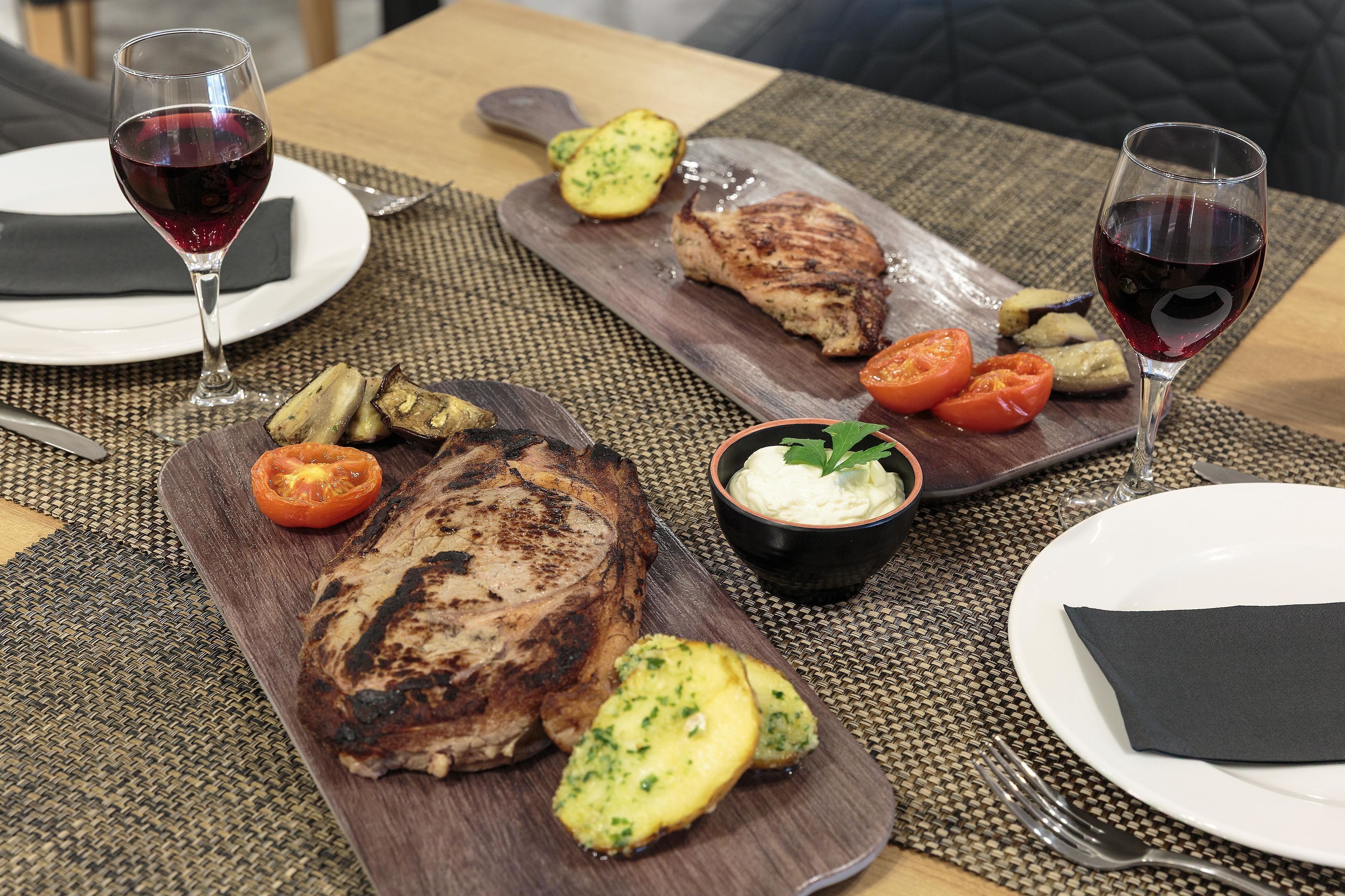 Una mesa de comedor con dos platos de comida, dos copas de vino tinto y un bol de salsa.