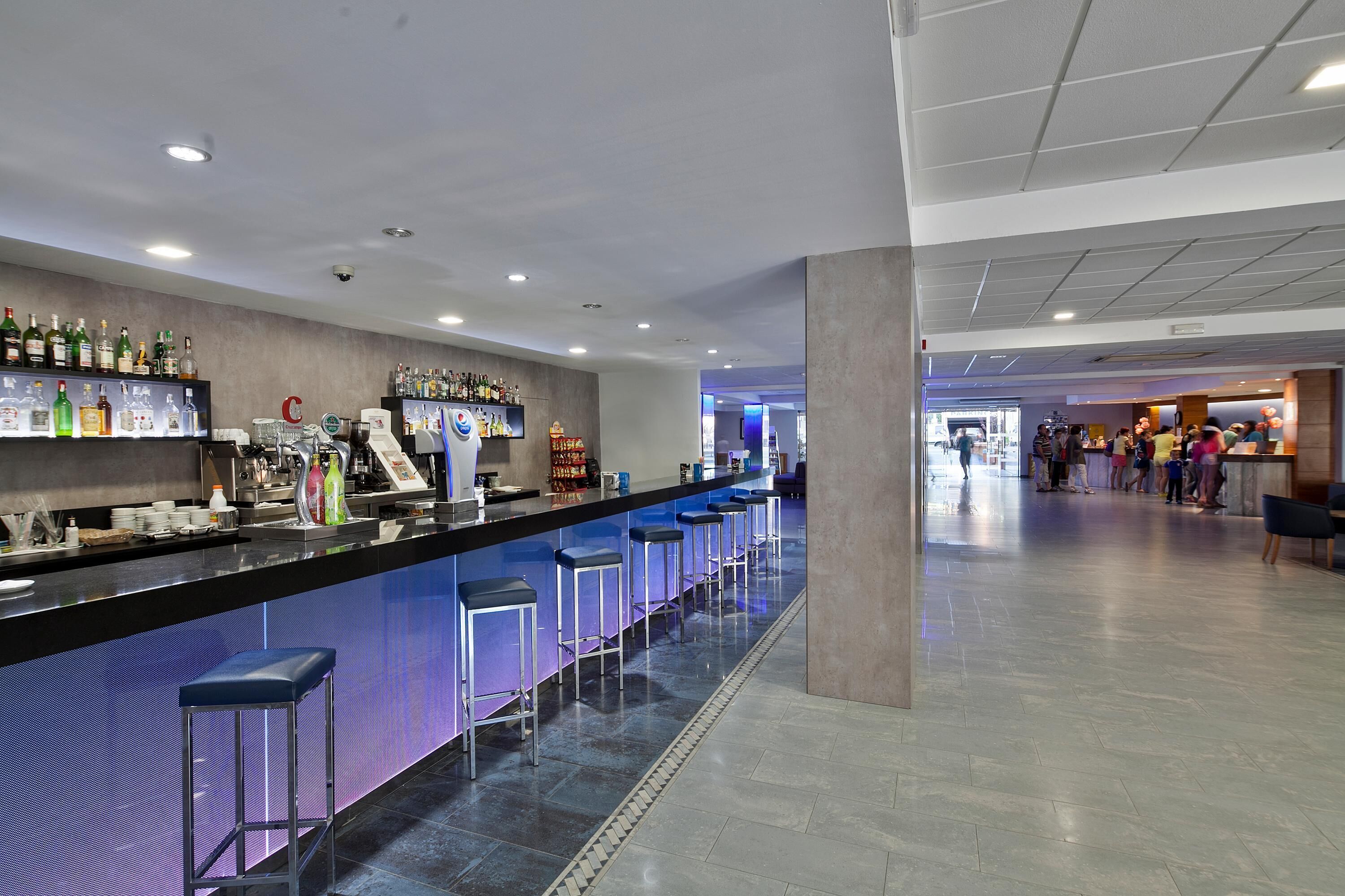 Zona de bar con taburetes, una barra con varias botellas y piso de baldosas.