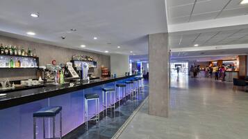 Zona de bar con taburetes, una barra con varias botellas y piso de baldosas.