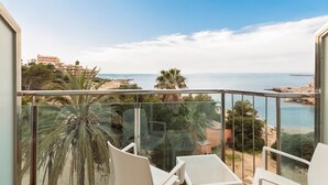 Un balcón con vista al mar, palmeras y edificios a lo lejos.