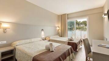 A hotel room with two beds, a desk, and a window with a view of trees.