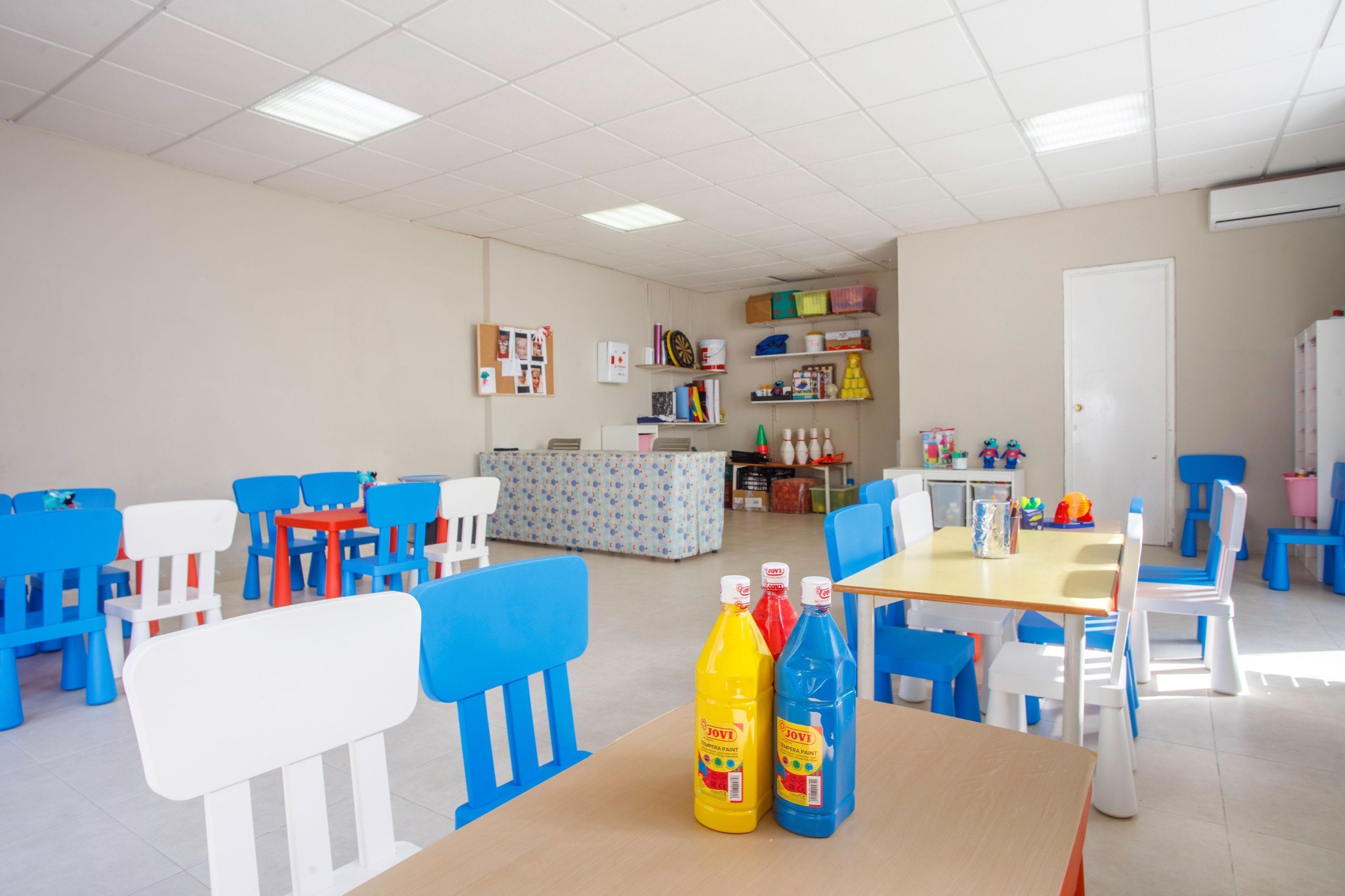 Un aula con mesas y sillas, materiales educativos y dos botellas de zumo Jovi sobre una mesa.