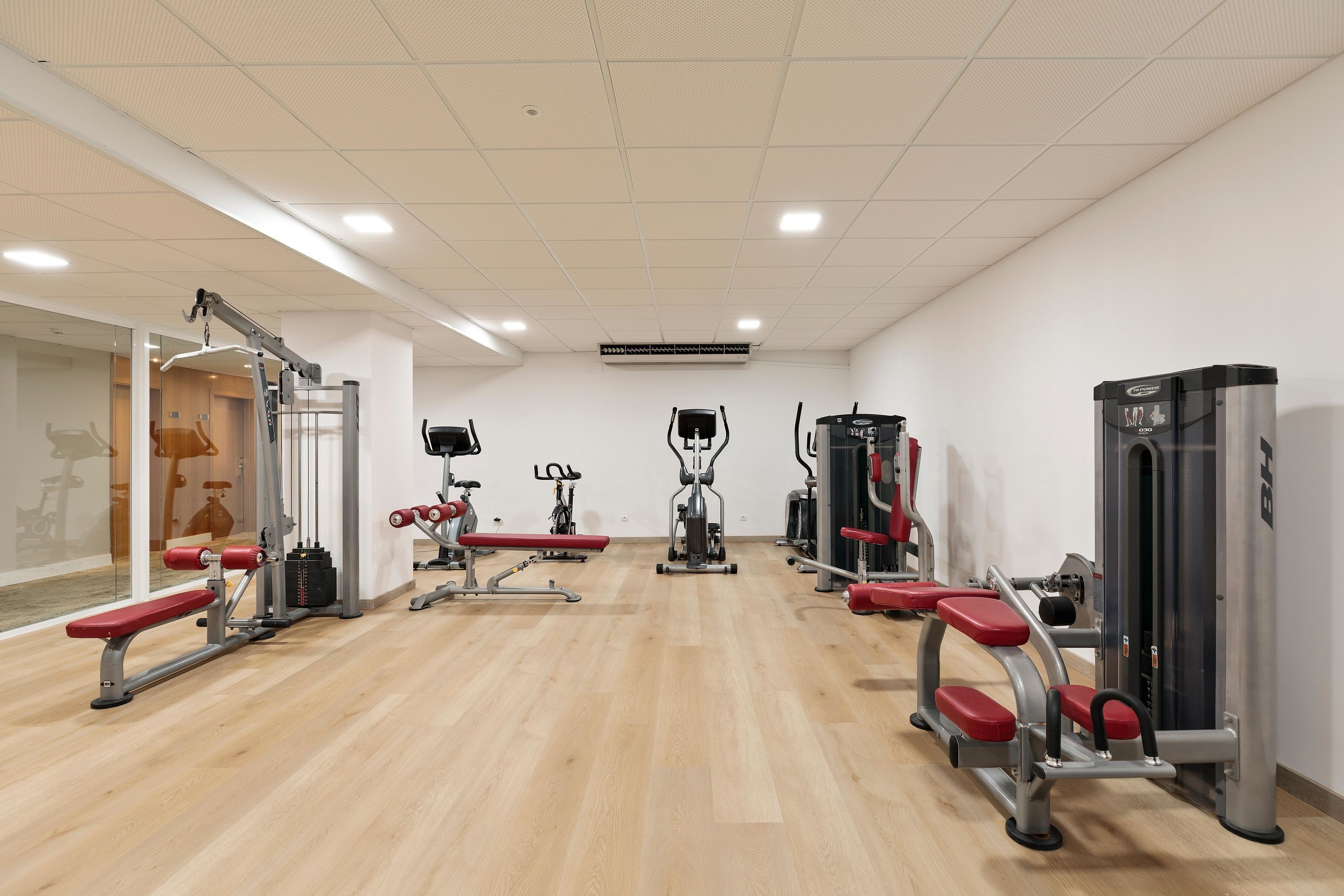 Un gimnasio con equipo de ejercicio, suelo de madera y paredes blancas.