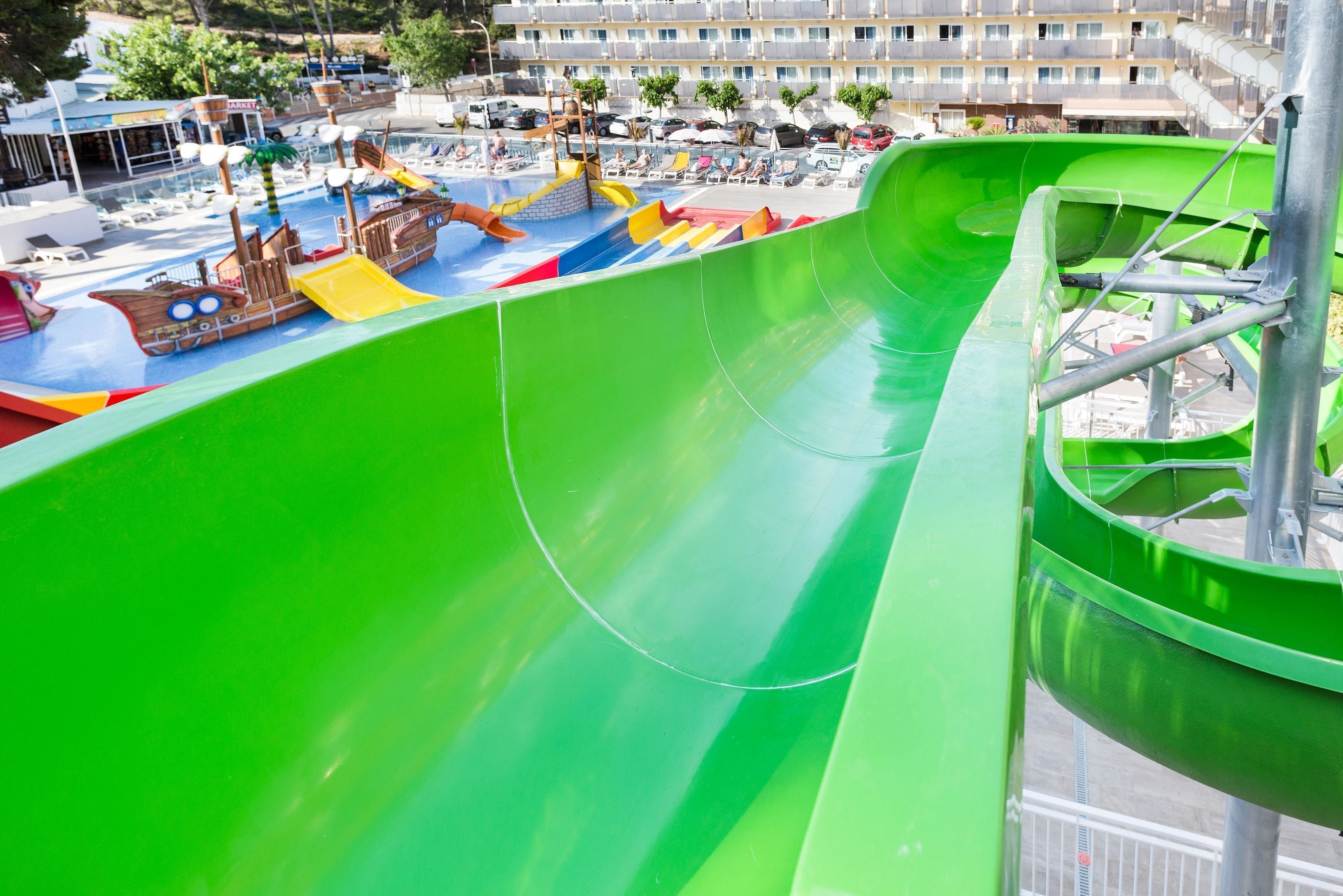 Um parque aquático com um escorregador verde, área de recreação em formato de navio pirata e uma piscina.