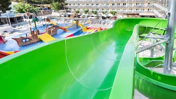 Um parque aquático com um escorregador verde, área de recreação em formato de navio pirata e uma piscina.