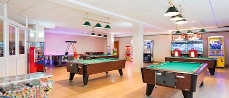 Sala de billar con múltiples mesas de billar, juegos de arcade y un interior luminoso y bien iluminado.