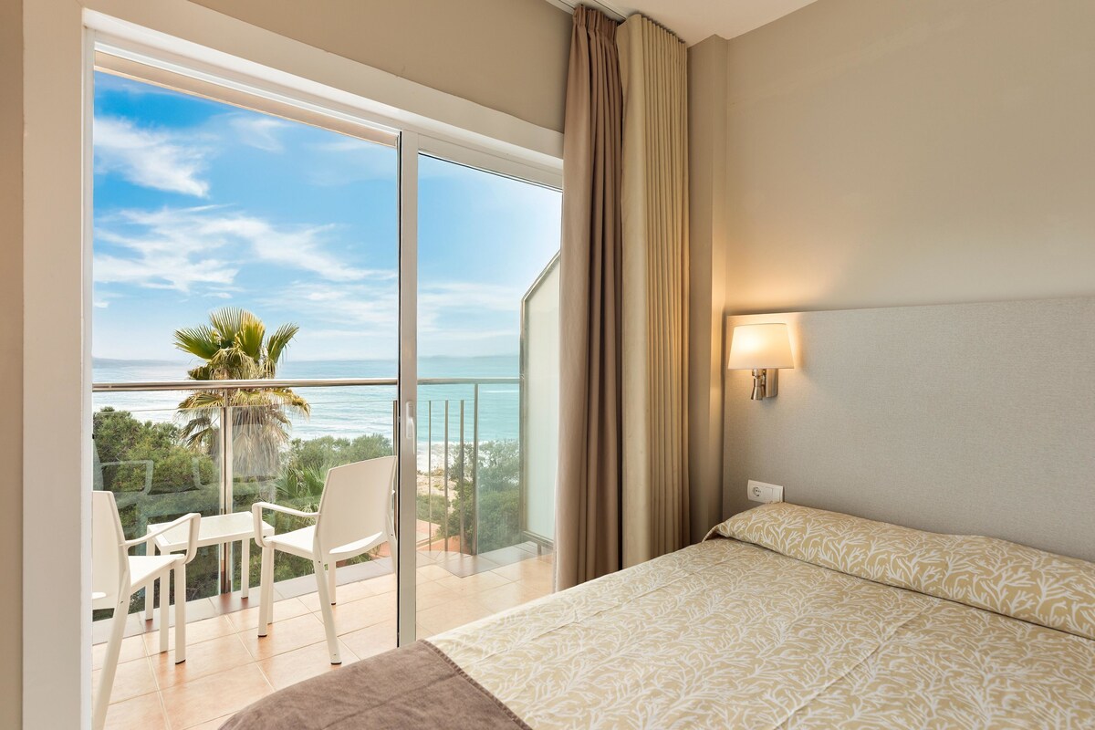 A hotel room with a balcony, a bed, a chair, and a view of the ocean.