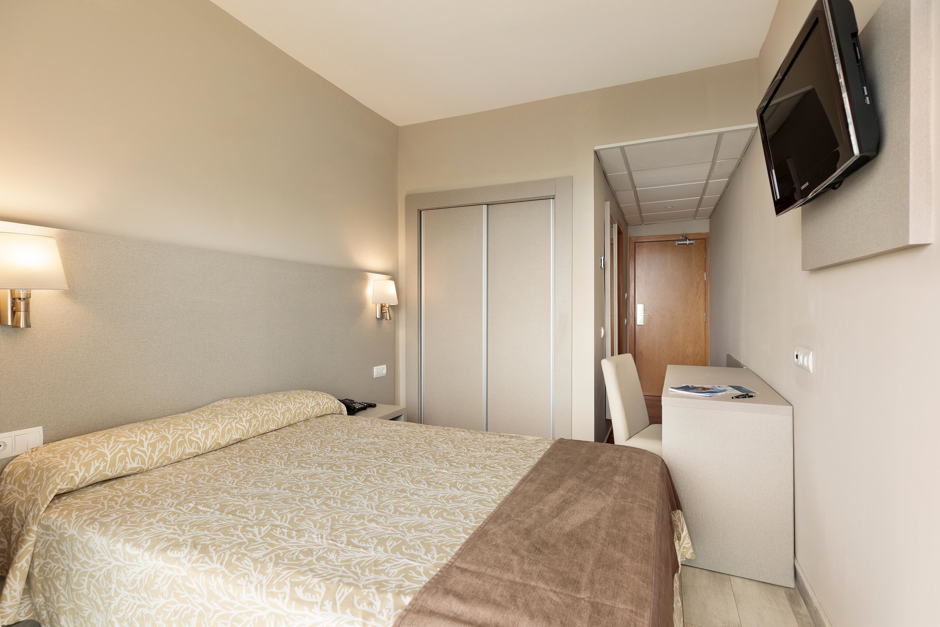 Una habitación de hotel con cama, mesita de noche, lámpara, televisor y escritorio con silla.
