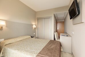 Una habitación de hotel con cama, mesita de noche, lámpara, televisor y escritorio con silla.