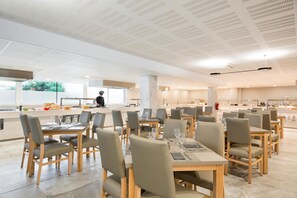 Un comedor moderno con varias mesas y sillas, una cocina al fondo y un techo con diseño de cuadrícula.