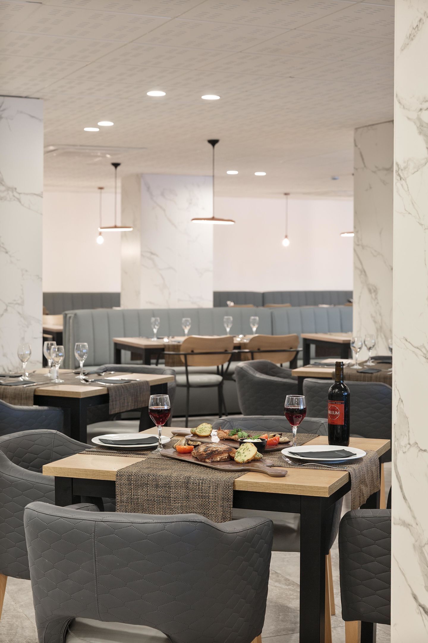 Un interior de restaurante con paredes de mármol, mesas de madera, sillas acolchadas e iluminación colgante.