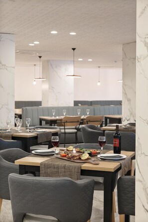 A restaurant interior with marble walls, wooden tables, cushioned chairs, and hanging pendant lights. - Hotel Best Cap Salou (Salou)
