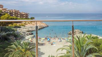 Vista de playa con cielo despejado, costa rocosa y un edificio al fondo.