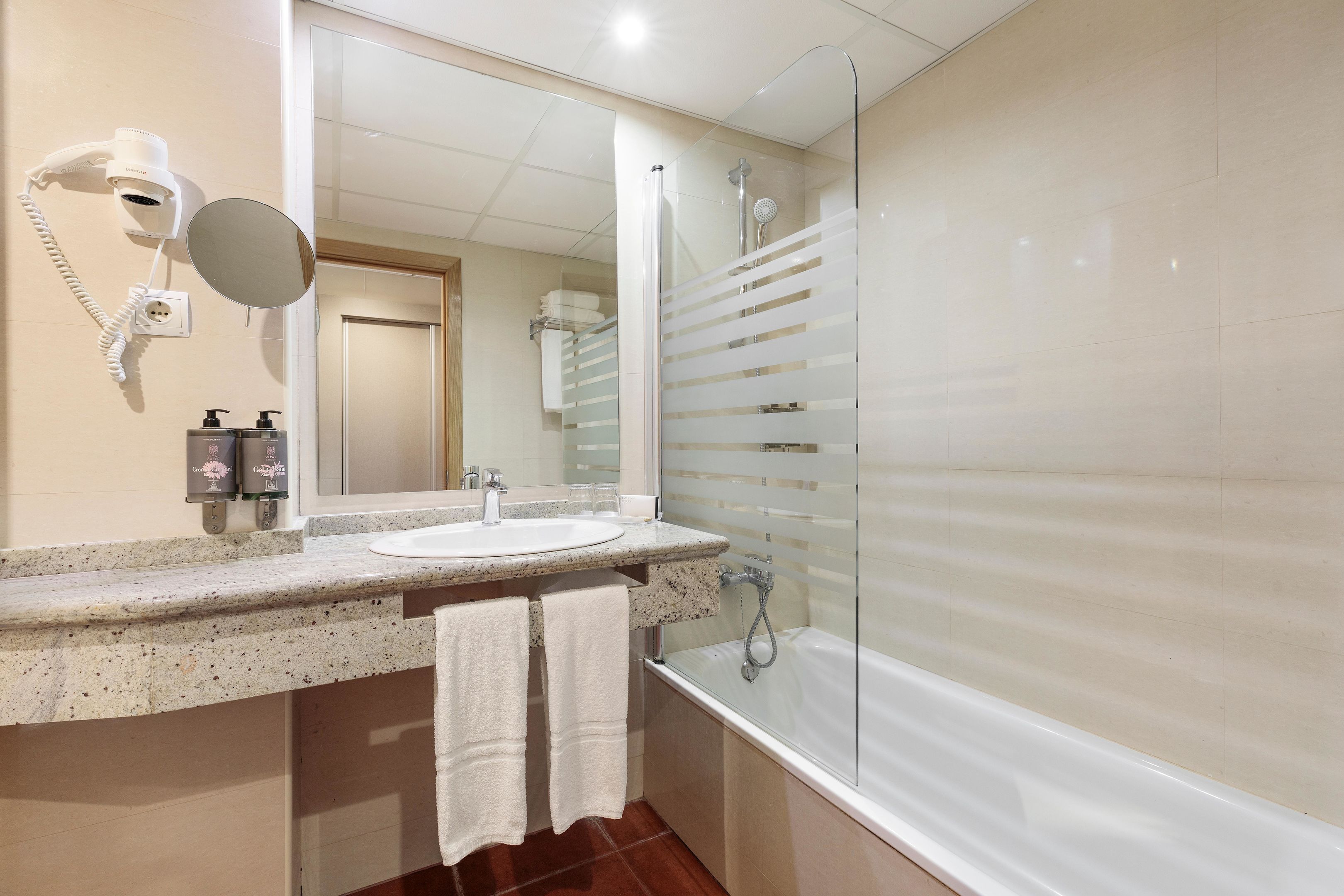 A bathroom with a sink, mirror, hairdryer, and shower.