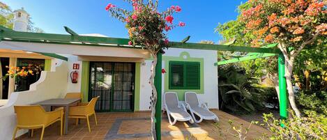 Un patio con mobiliario exterior, una pérgola verde y un edificio blanco con puerta verde.
