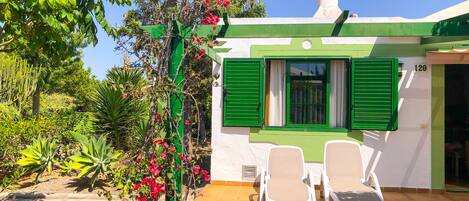 Una villa con fachada verde y blanca, una chimenea y dos sillones blancos en el jardín.