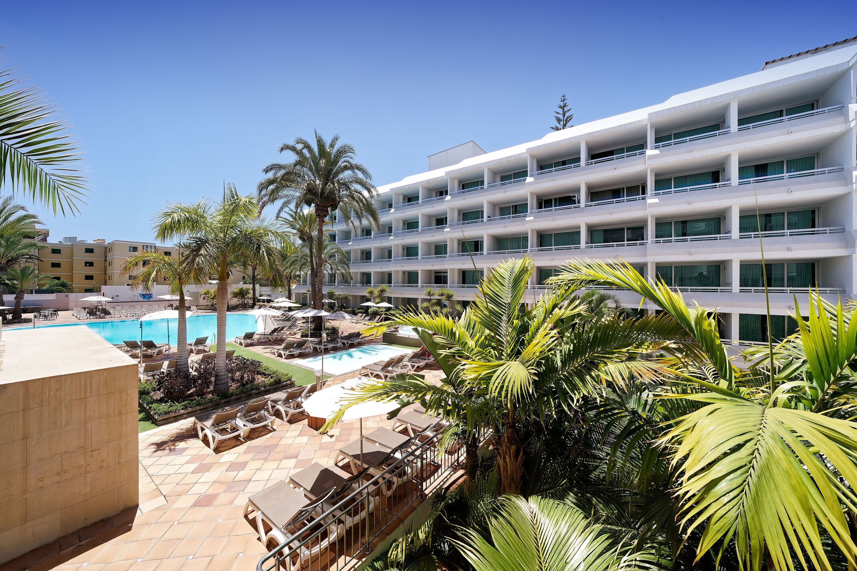 Un hotel con piscina, palmeras y un edificio de varios pisos.