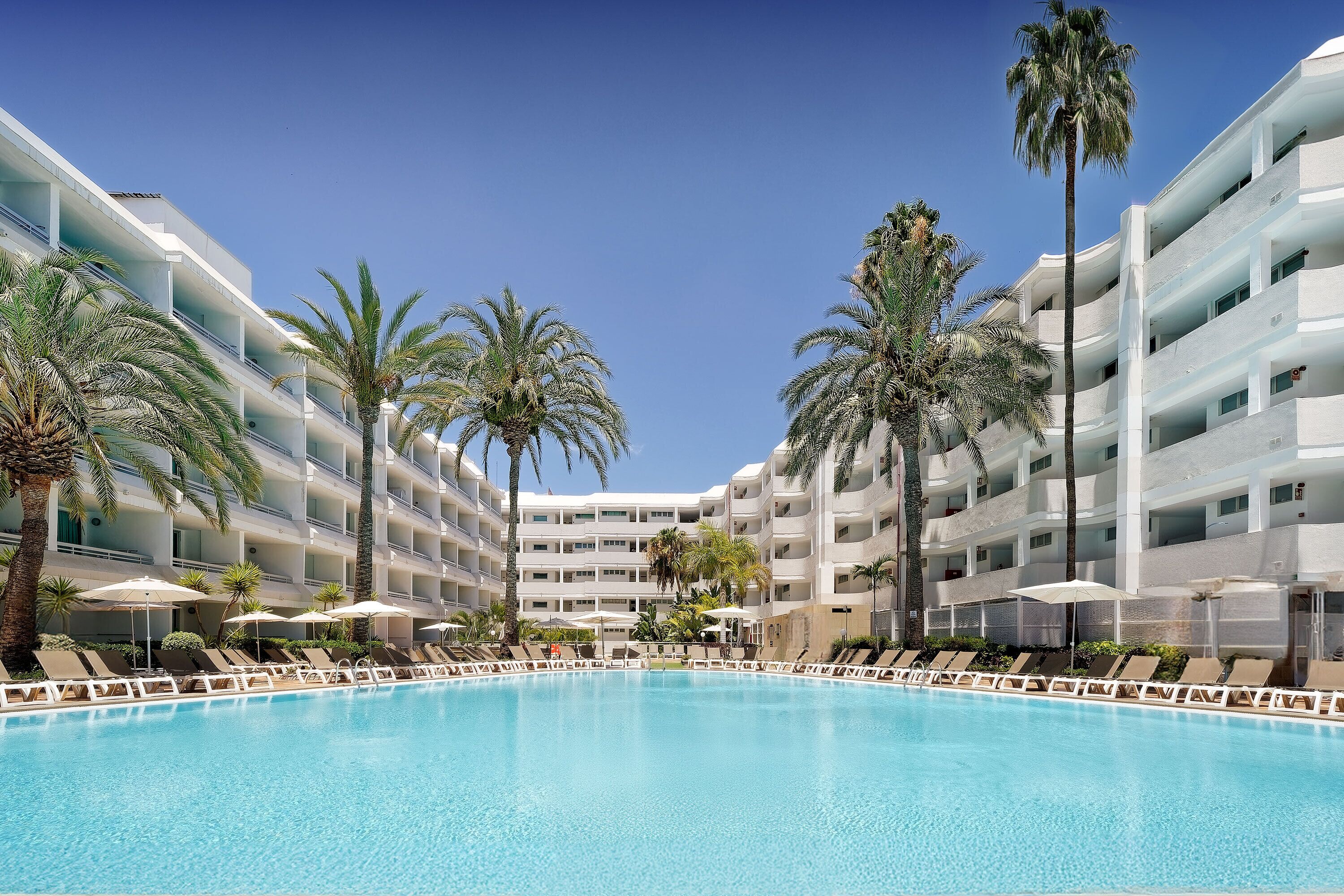 Una piscina al aire libre, sombrillas, sillones reclinables de piscina