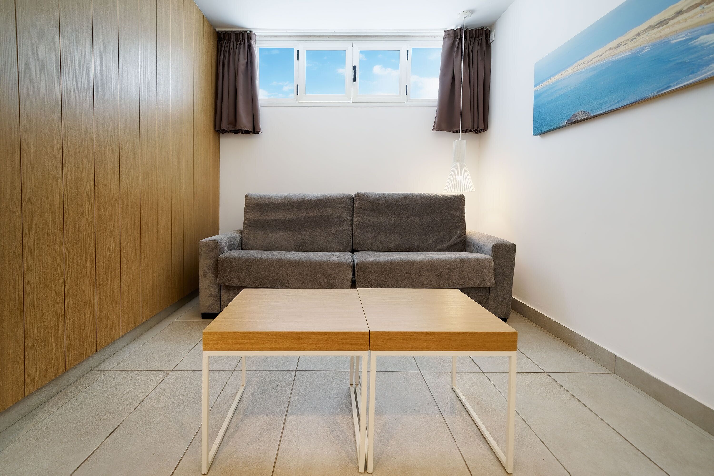 A room with a wooden wardrobe, a grey sofa, and a wooden table.