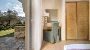 A bedroom with a stone wall, a wooden door, and a view of the garden. - Alkion Hotel (Kassandra)