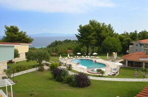 Área da piscina com espreguiçadeiras e guarda-sóis, rodeada por vegetação e vista para o mar.