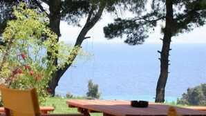 An outdoor seating area with wooden tables and chairs, overlooking a body of water. - Alkion Hotel (Kassandra)