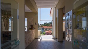 A corridor with a tiled floor leading to an outdoor area with a view of buildings and trees. - Alkion Hotel (Kassandra)