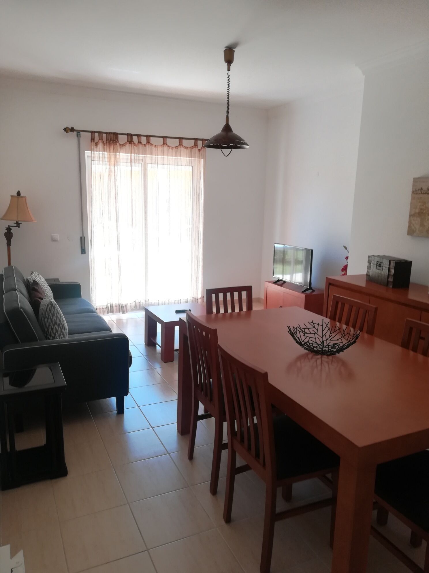 A living room with a sofa, a dining table with chairs, a television, and a ceiling fan.