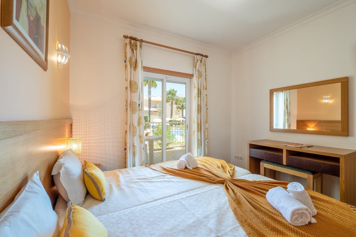 A hotel room with a bed, a desk, a mirror, and a window with curtains.