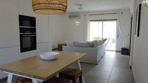 A modern kitchen with white cabinets, a wooden dining table, and a wicker pendant light. - Jardins Vale de Parra (Albufeira)
