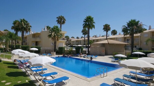 A pool area with lounge chairs and umbrellas, surrounded by palm trees and hotel buildings. - Jardins Vale de Parra (Albufeira)