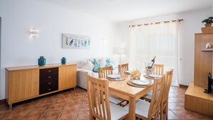 A dining area with a wooden table, chairs, a cabinet, and a sofa. - Jardins Vale de Parra (Albufeira)