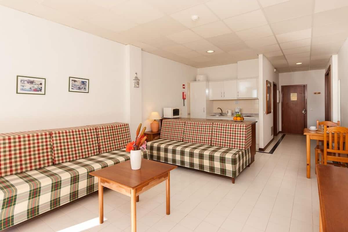 A modern living room with a sofa, a coffee table, and a kitchen area with cabinets and a countertop.