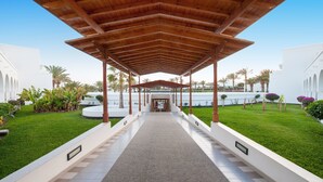 Un pasillo cubierto que conduce a un edificio de estilo arquitectónico moderno, rodeado de vegetación cuidada y palmeras.