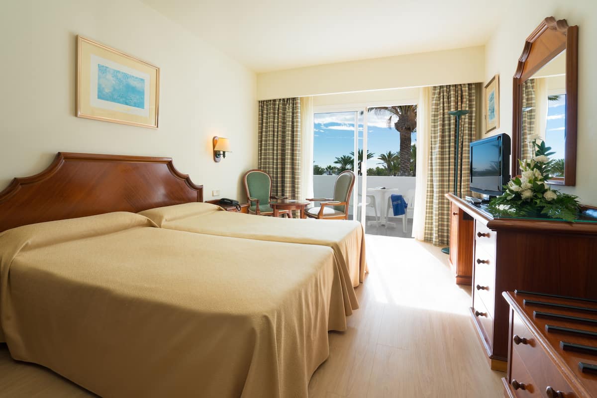 A hotel room with two beds, a television, a desk, and a view of the ocean.