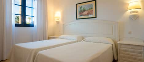 A hotel room with two beds, a nightstand, a lamp, and a painting on the wall.