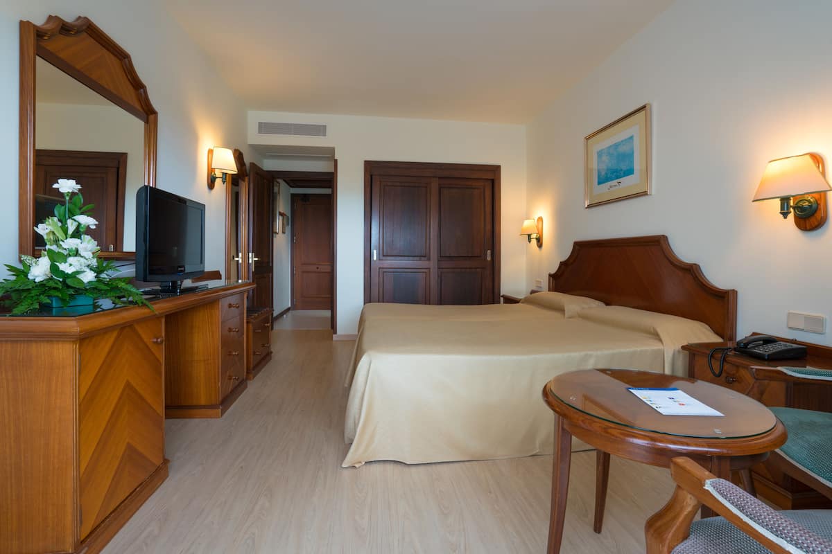 A hotel room with a bed, bedside table, desk, chair, TV, and a mirror.