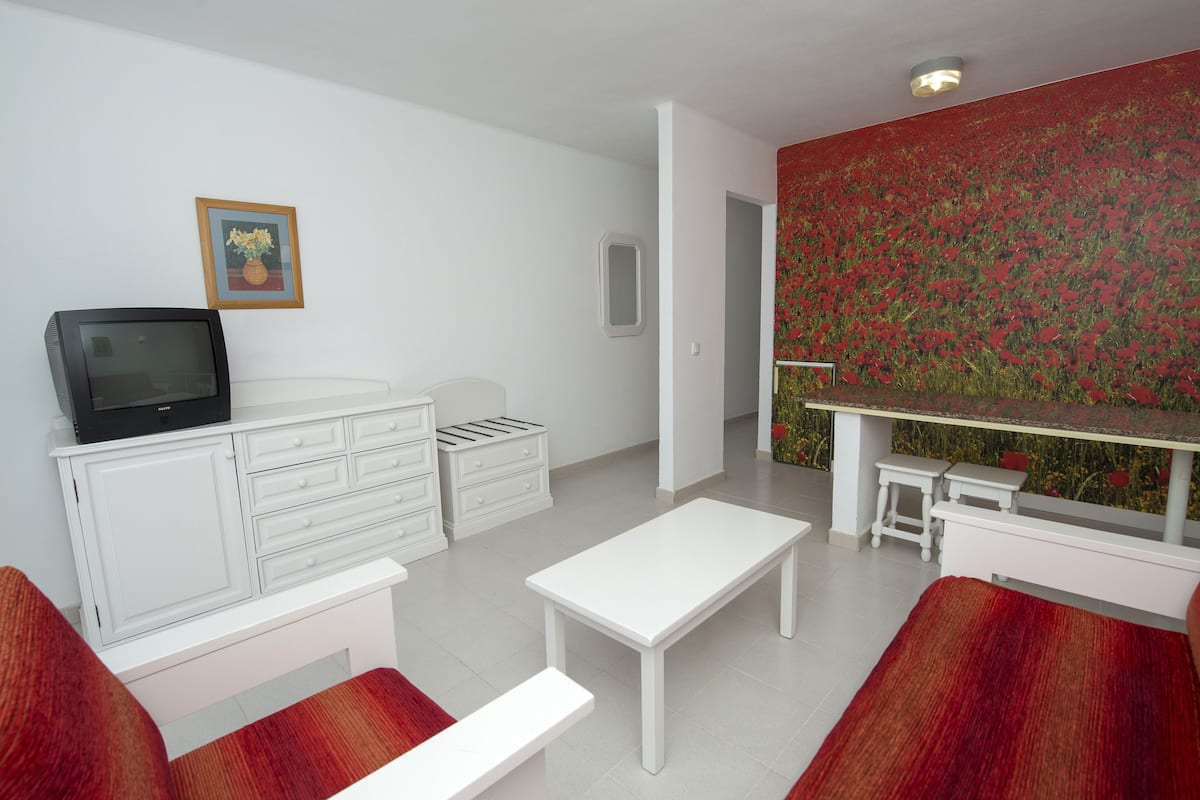A modern living room with a white sofa, a white coffee table, a television on a cabinet, and a vibrant floral wallpaper.