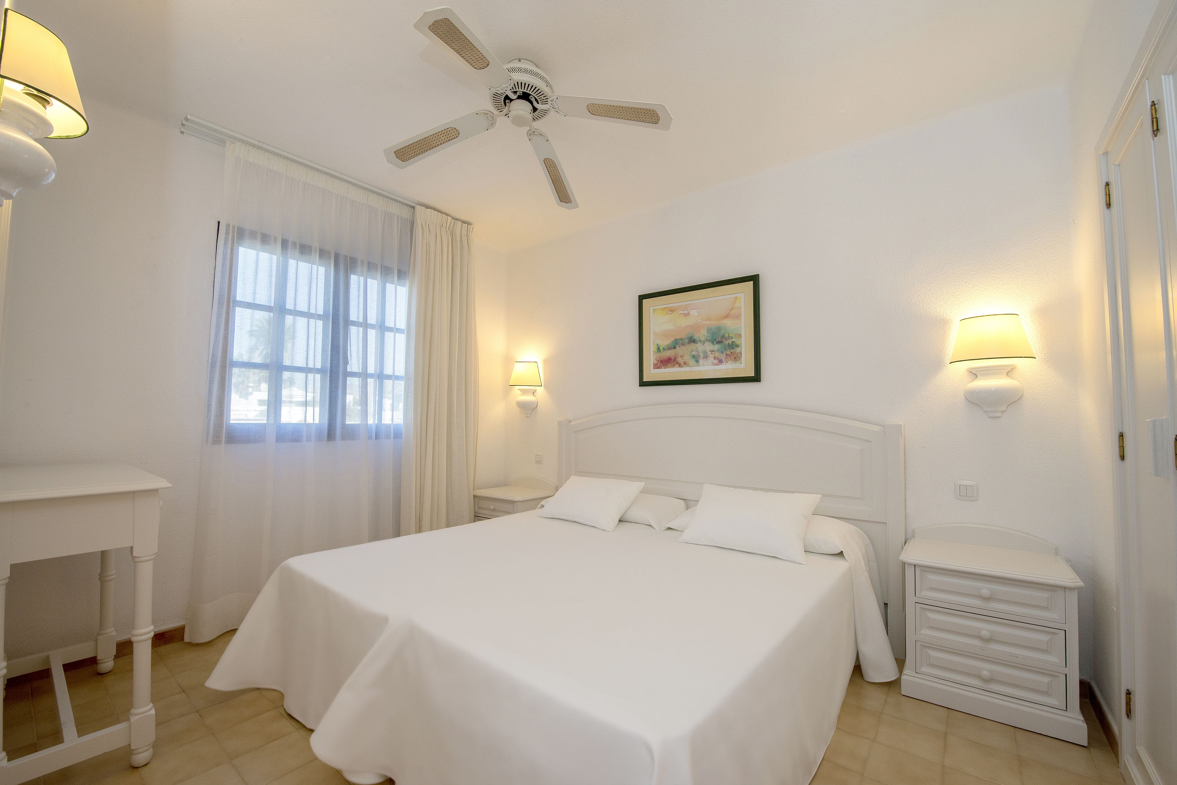 A neatly arranged bedroom with a bed, bedside tables, a ceiling fan, and a window with curtains.