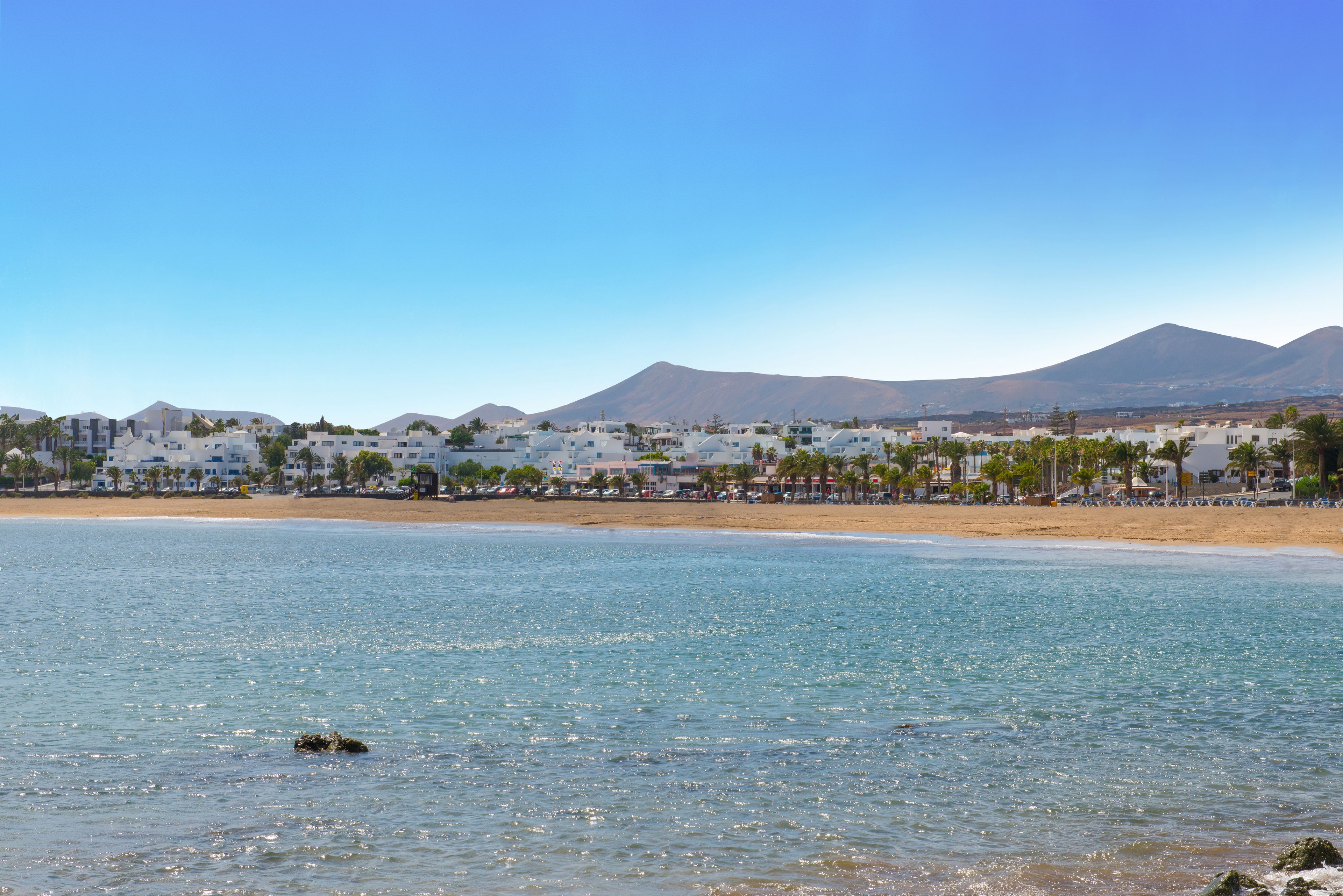 A coastal town with a beach, clear blue sky, and mountains in the background.
