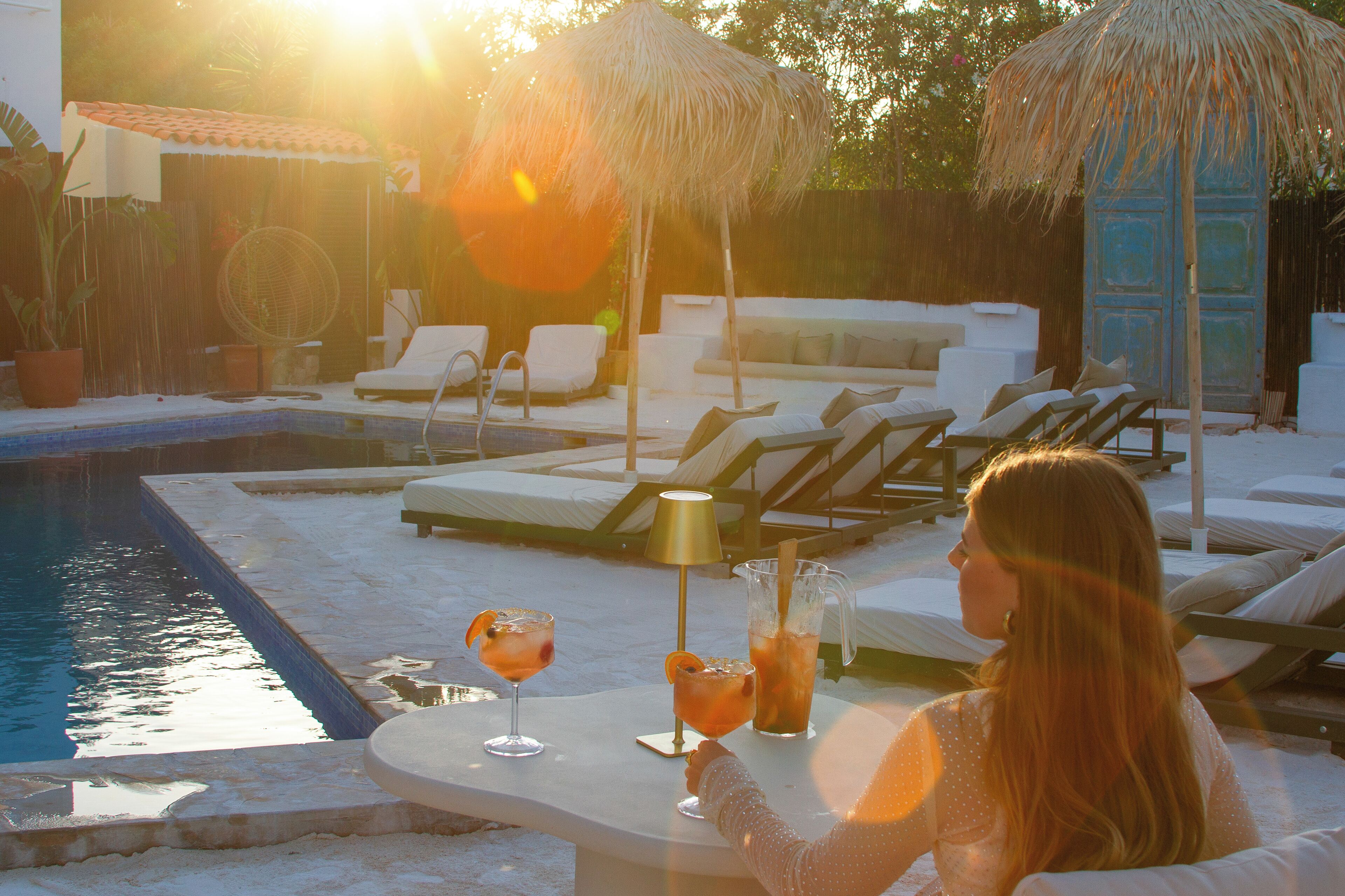 Un espace aménagé au bord de la piscine, avec des chaises longues, une table où sont servis des boissons et un parasol en feuilles de palmier.