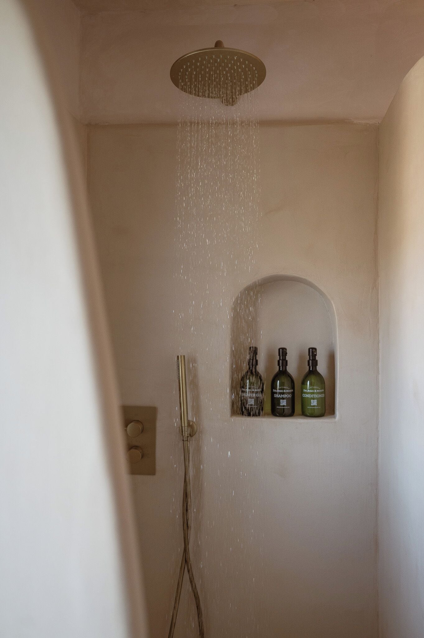 A shower with a rain showerhead and three bottles of shampoo, conditioner, and body wash on the wall.