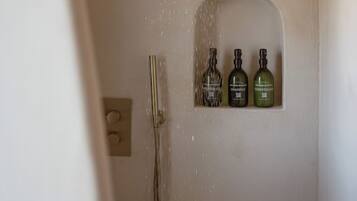 A shower with a rain showerhead and three bottles of shampoo, conditioner, and body wash on the wall.