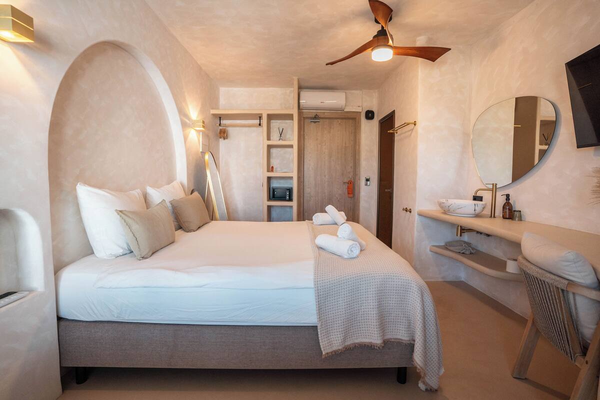 Un dormitorio con cama, mesita de noche, espejo, ventilador de techo y estante empotrado.
