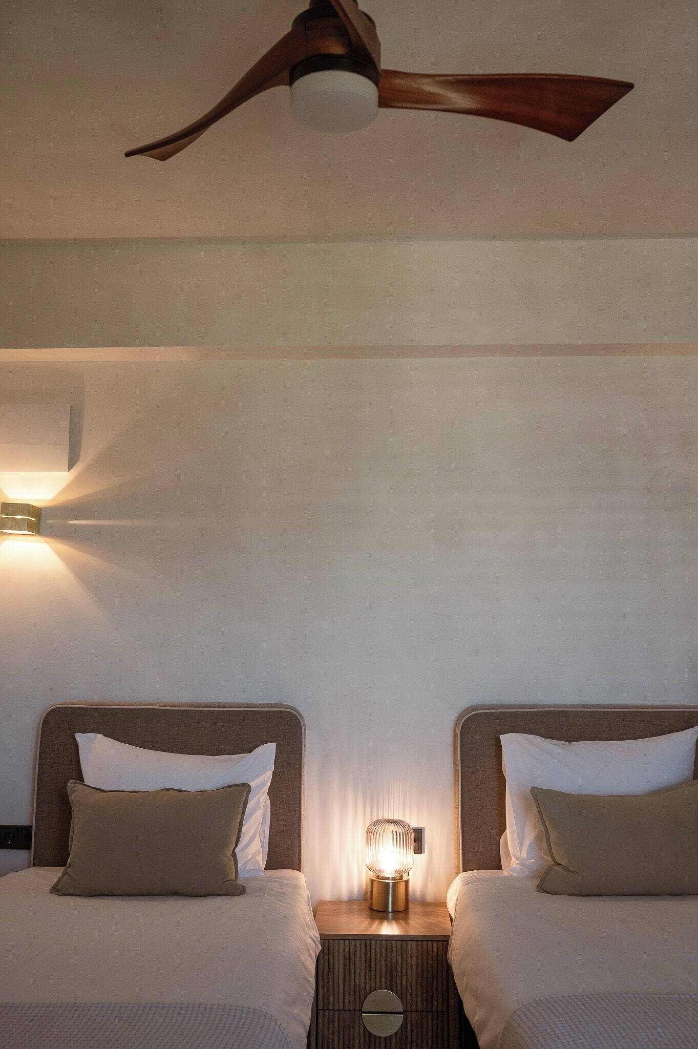 Habitación de hotel con dos camas, un ventilador de techo y una mesita de noche con lámpara.