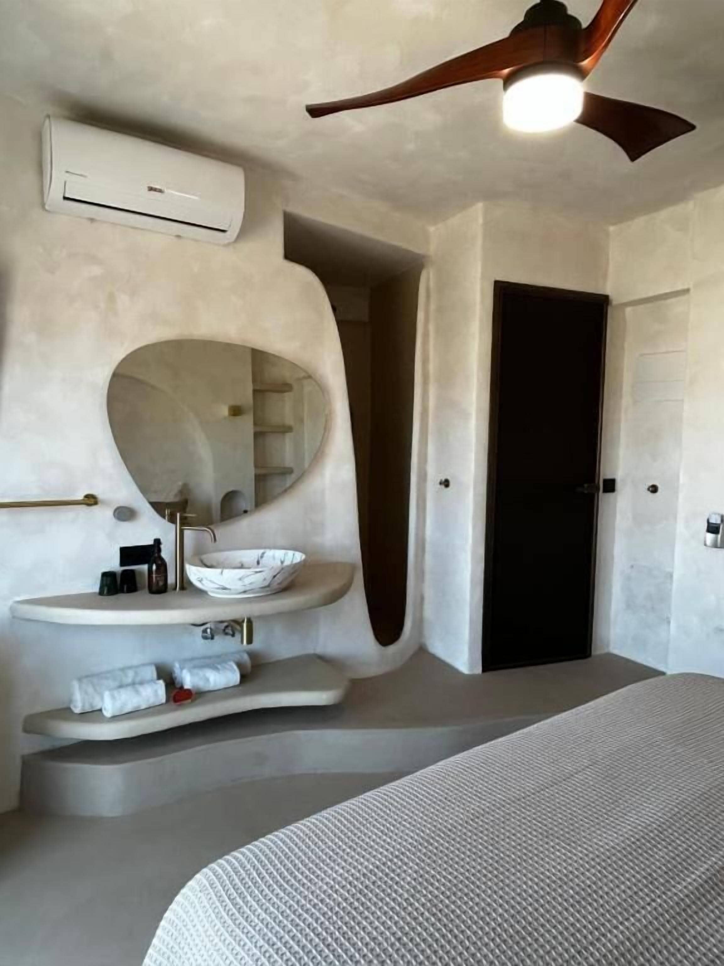 Een moderne badkamer met een vrijstaand wastafelmeubel, een ronde spiegel en een plafondventilator.