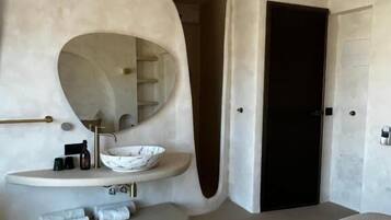 Un baño moderno con lavamanos independiente, un espejo redondo y un ventilador de techo.