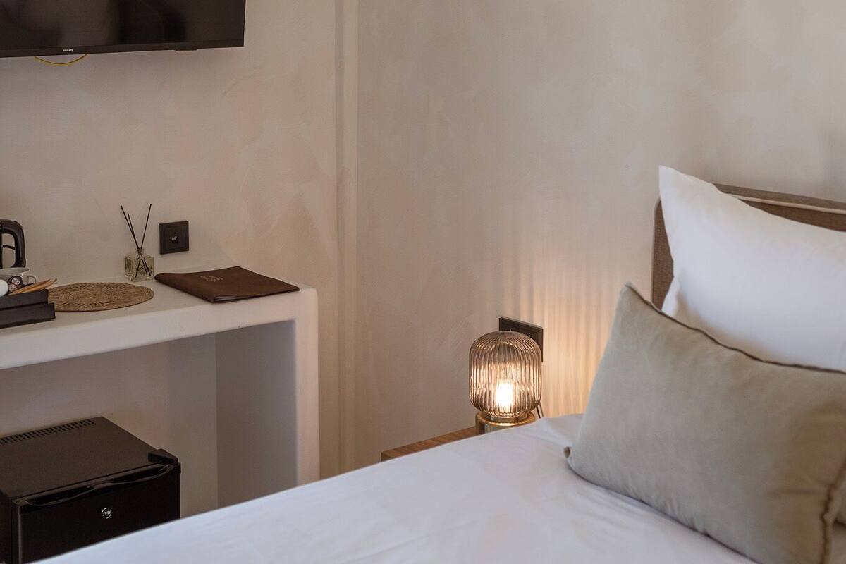 Habitación de hotel con cama, escritorio con una computadora portátil, televisión en la pared y lámpara de noche.
